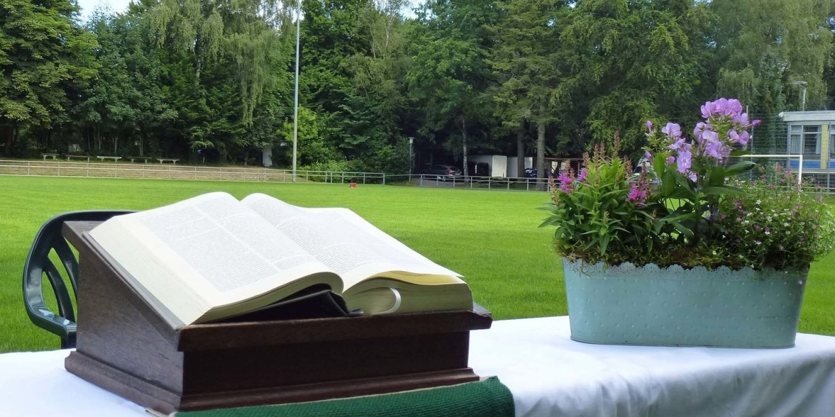 Aufgebauter Altar mit Bibel und Blumenschmuck auf einem Fußballfeld, © Karen Diehn Aufgebauter Altar mit Bibel und Blumenschmuck auf einem Fußballfeld, © Karen Diehn