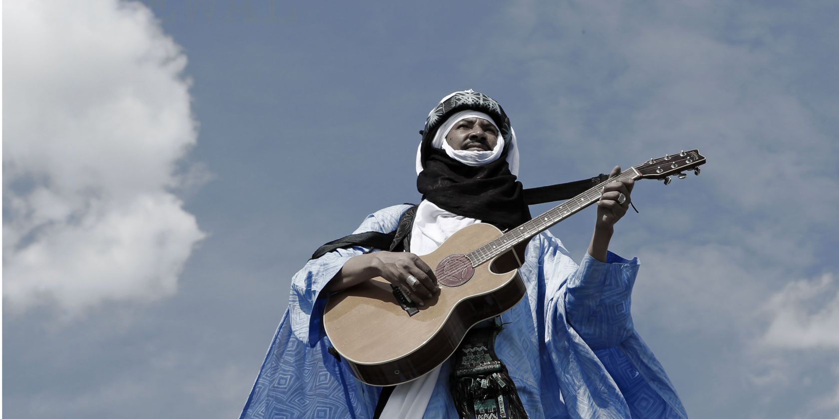Alhousseini Anivolla is standing on a rooftop with a guitar. The sky can be seen in the background., © Alhousseini Anivolla Alhousseini Anivolla is standing on a rooftop with a guitar. The sky can be seen in the background., © Alhousseini Anivolla
