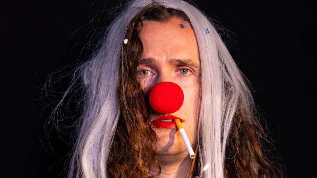 A person in a clown costume has a cigarette in their mouth. The cigarette is lit., © Mayra Wallraff A person in a clown costume has a cigarette in their mouth. The cigarette is lit., © Mayra Wallraff