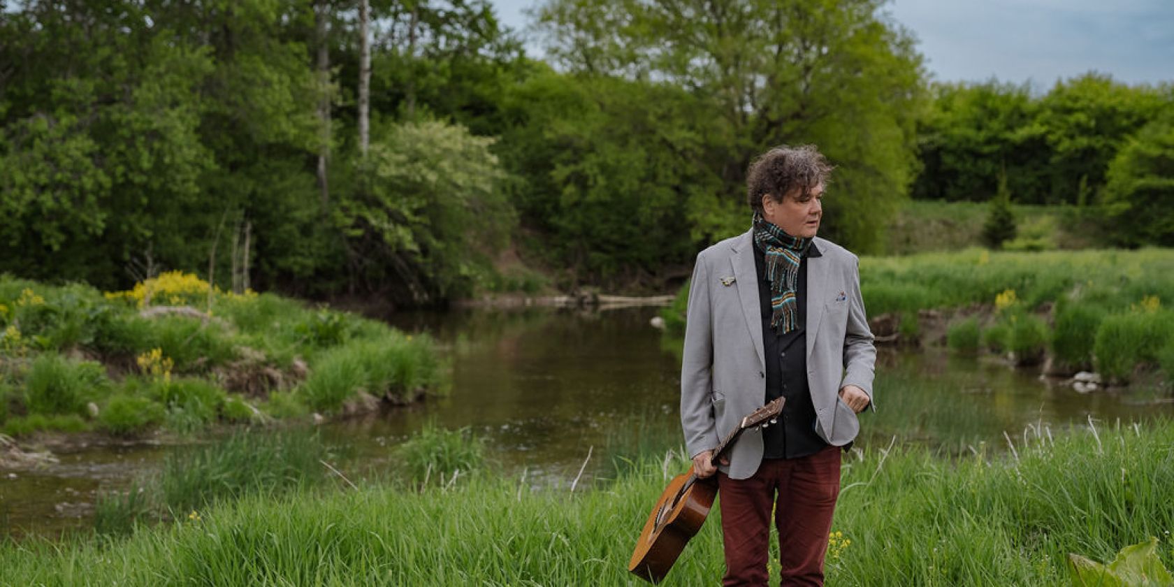 Ron Sexsmith steht in einer grünen Landschaft und hält seine Gitarre in der Hand., © Budde Talent Agency GmbH Ron Sexsmith steht in einer grünen Landschaft und hält seine Gitarre in der Hand., © Budde Talent Agency GmbH
