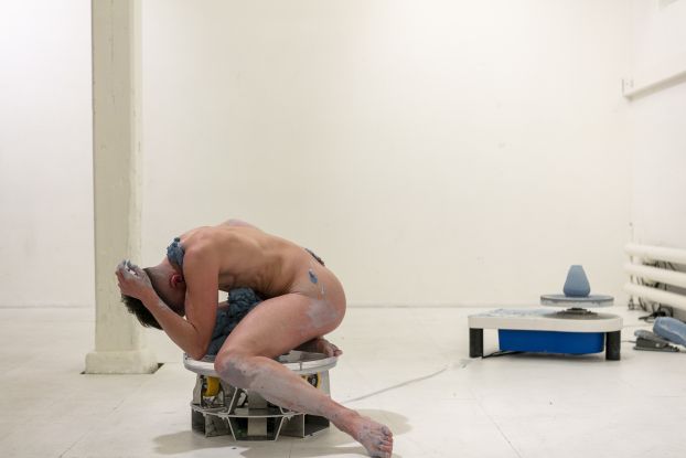 Excerpt from Simone Aughterlony's performance "Hand Job." A naked person sits with their head buried in their hands, covered in a clay-like substance, on a stool and can only be seen from the side., &copy; Peter Hauser