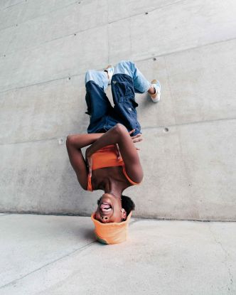 Eine junge Frau die kopf&uuml;ber an einer Wand lehnt und Grimassen schneidet, &copy; Foto: Fellipe Ditadi / Unsplash+