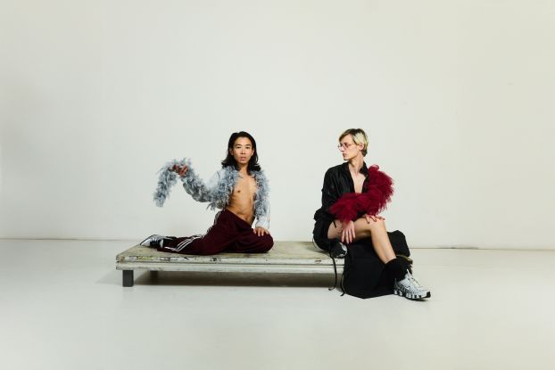 Two performers on a small platform. They wear revealing dark clothing and each wear a feather boa around their shoulders., © Julian Baumann