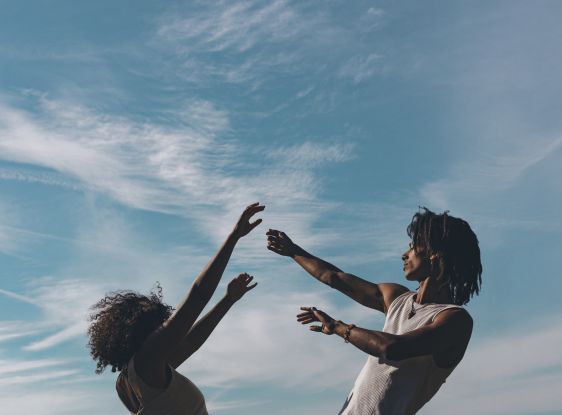 Two people raise their arms toward the sky, silhouetted against a blue sky with wispy clouds., © Ashley.C Twumasi /  Anam (Lukas Lubisia)