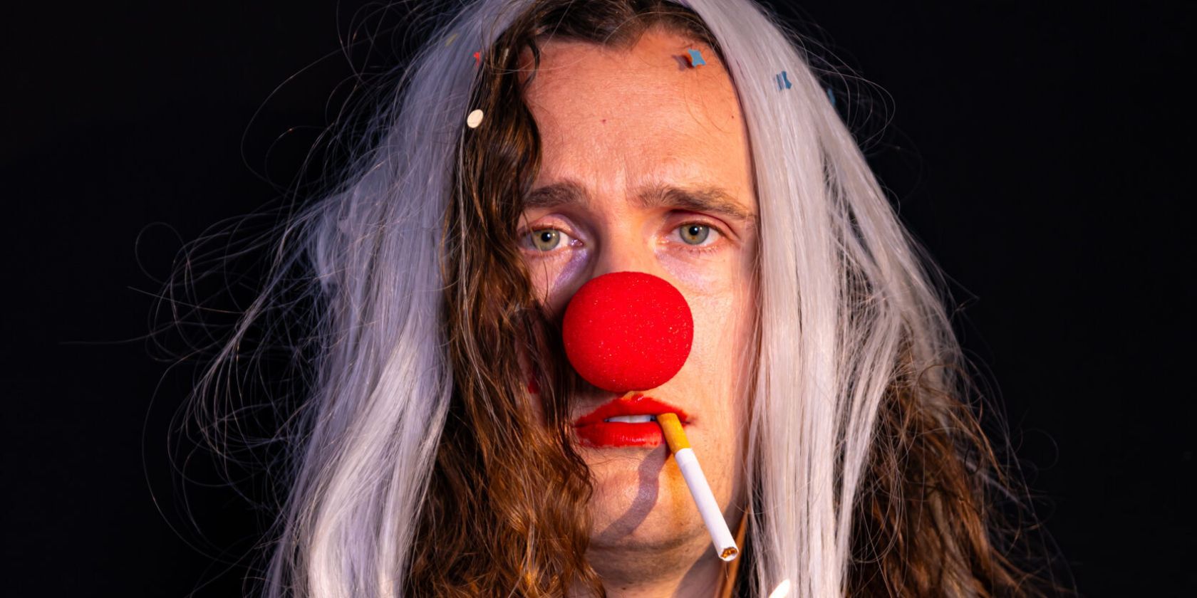 A person in a clown costume has a cigarette in their mouth. The cigarette is lit., &copy; Mayra Wallraff