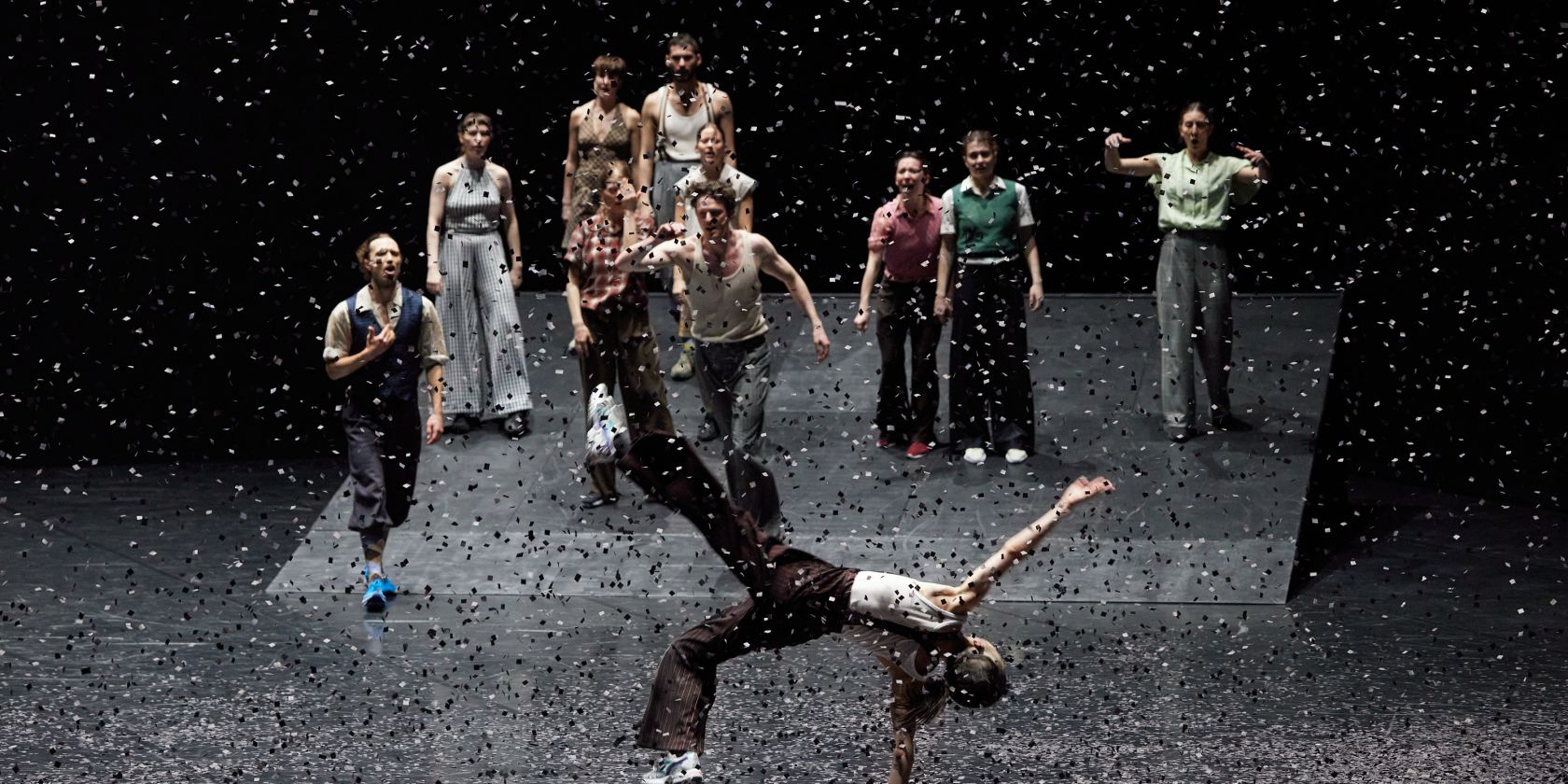 A group of dancers stands on a sloped stage while, in the foreground, one person balances impressively on one hand as confetti swirls through the air., © Dominik Mentzos