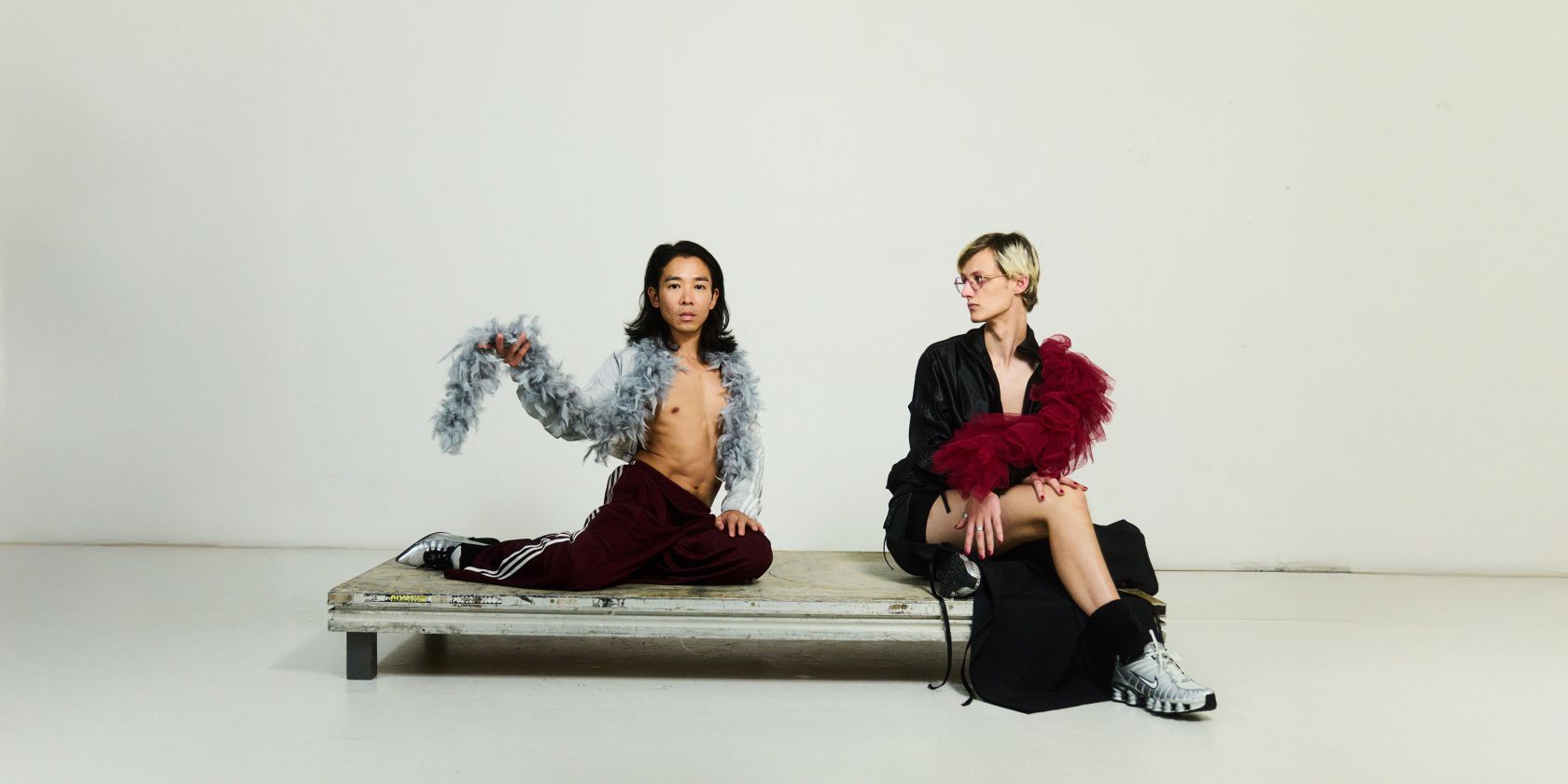 Two performers on a small platform. They wear revealing dark clothing and each wear a feather boa around their shoulders., © Julian Baumann
