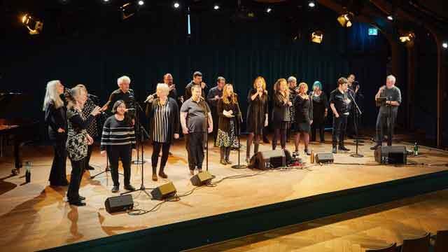 Eine Gruppe von Menschen steht auf einer B&uuml;hne und singt gemeinsam in Mikrofone., &copy; Singing With Sounddrops