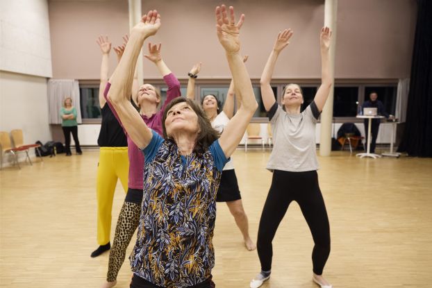 Five people are standing behind each other in a dance studio, each with both arms stretched toward the ceiling. They are wearing colorful sportswear and their eyes are directed toward the ceiling., &copy; Julie Nagel